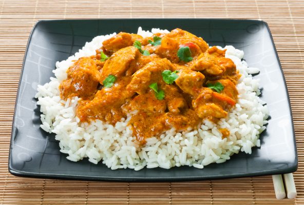 Chicken curry and rice on black plate on bamboo matting